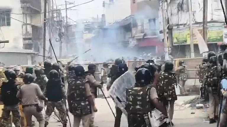 فسادات کے دوران پولیس اہلکار سڑک پر کھڑے ہیں، پس منظر میں دھواں اور تباہ شدہ عمارتیں ہیں۔