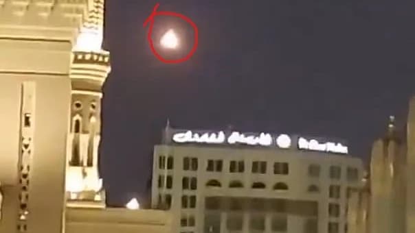 رات کے وقت ایک عمارت کے اوپر آسمان میں ایک روشن مثلثی چیز نظر آرہی ہے۔