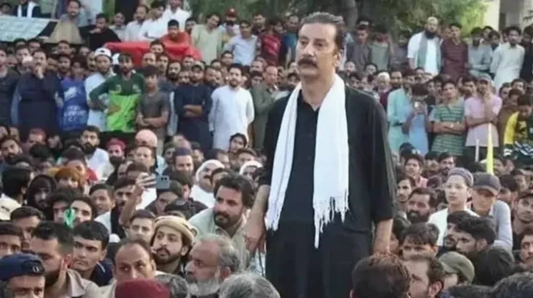 ایک شخص سیاہ لباس اور سفید شال پہنے ہوئے ہجوم کے درمیان کھڑا ہے۔
