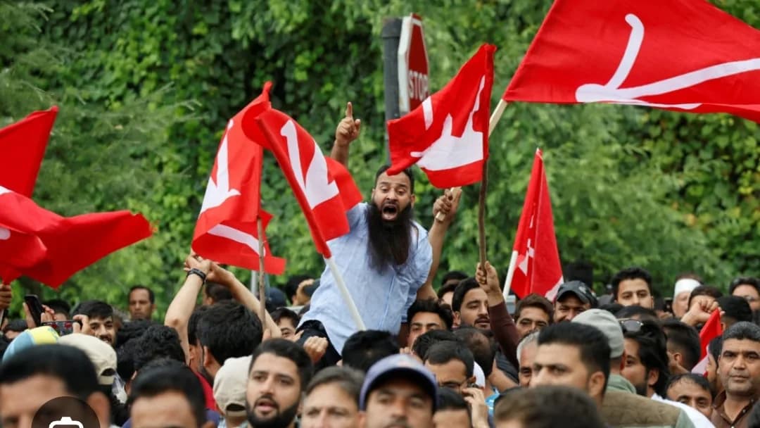 ایک داڑھی والا آدمی سرخ جھنڈے اٹھائے ہجوم کے درمیان کھڑا ہے۔