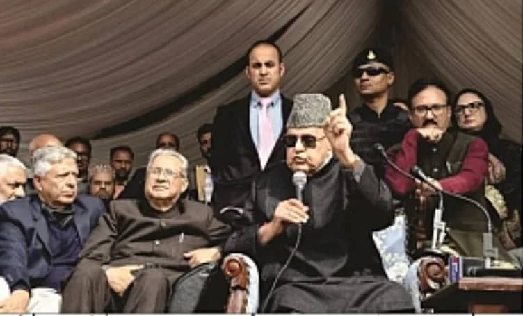 ایک بزرگ شخص مائیکرو فون پر بات کر رہا ہے، اس کے ساتھ دیگر افراد بھی بیٹھے ہیں۔