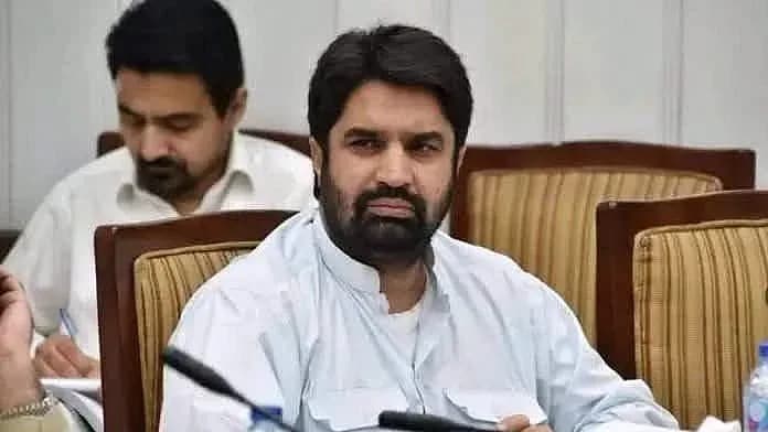 ایک داڑھی والا آدمی سفید قمیض پہنے کرسی پر بیٹھا ہے۔