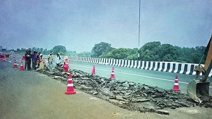سڑک کے کنارے کھڑے لوگ اور ایک کھدائی کرنے والا سڑک کی مرمت کر رہا ہے۔